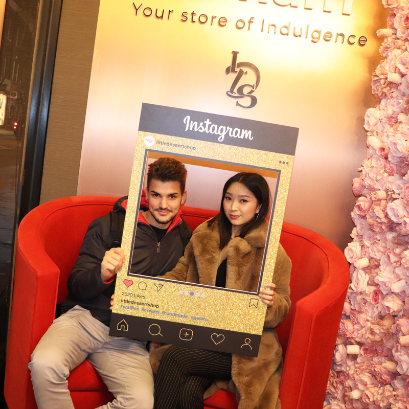 A Little Dessert Shop selfie frame with two customers holding it up for a picture