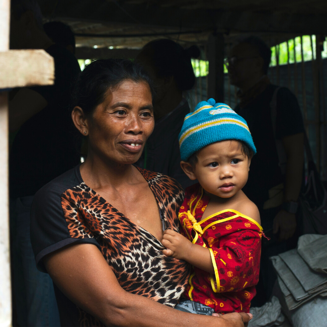 Charity Woman holding a young child who is wearing a red shirt and blue hat